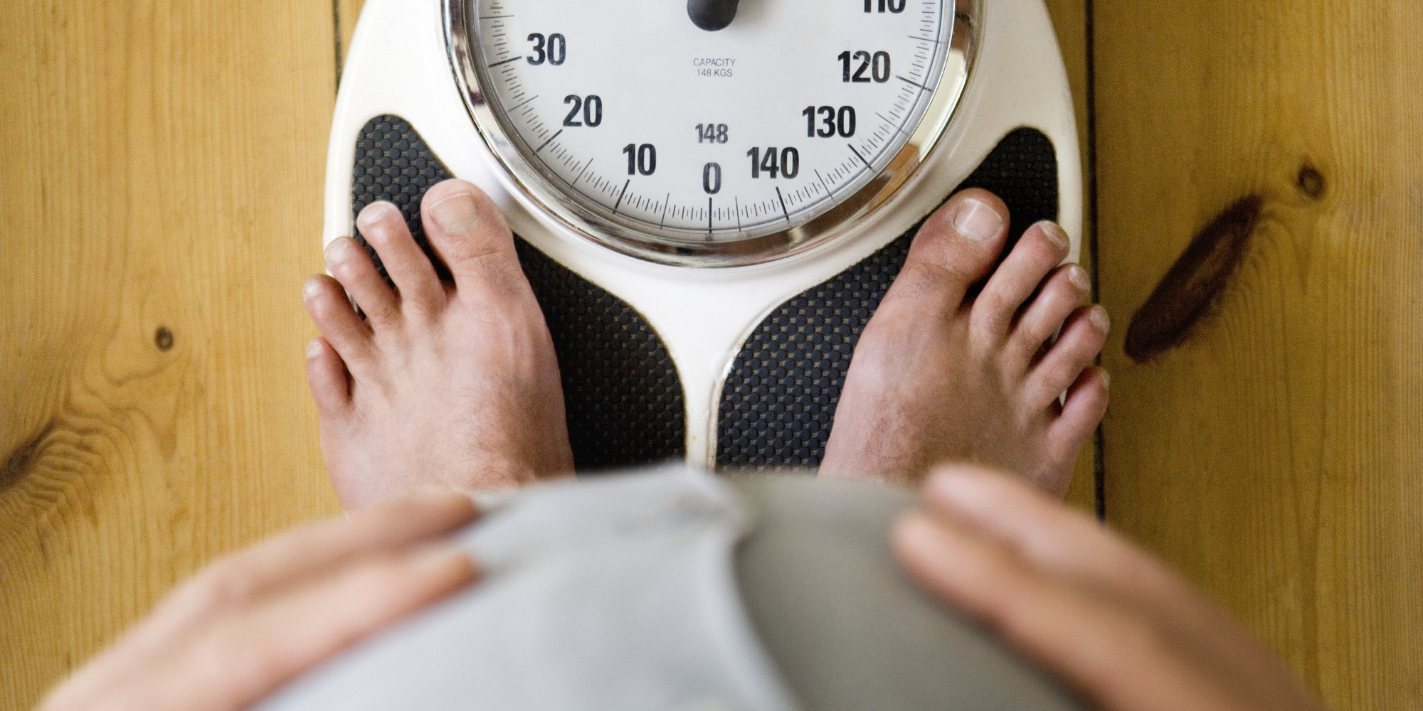 Man holding belly, with feet on weighing scales